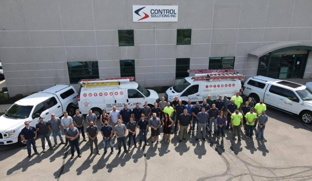 A throwback picture with Control Solutions employees posing in front of the Control Solution's office building with company vehicles